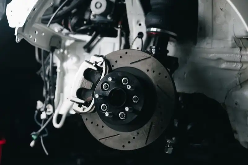 A drilled brake disc and caliper on a vehicle with the wheel removed